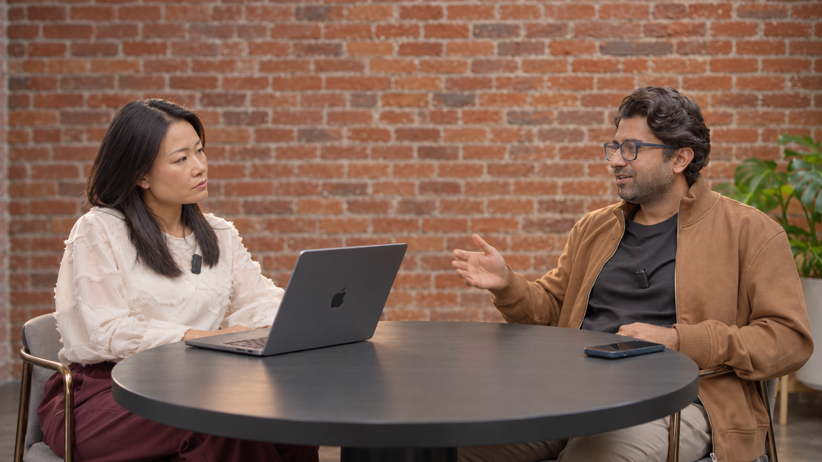 Two people in conversation during a Strange Machines interview, seated at a round table with a laptop